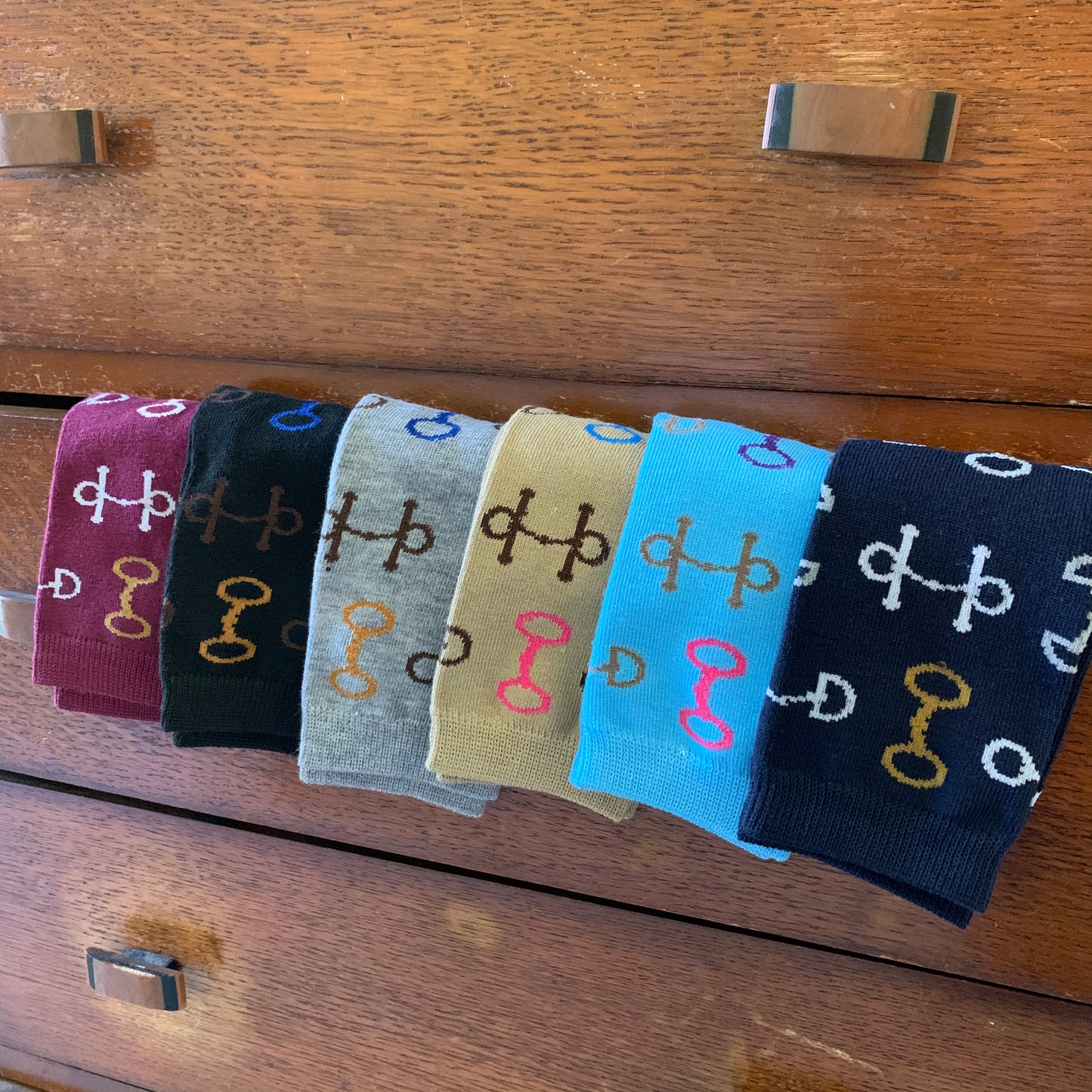 Socks in Maroon Black Grey Tan Aqua and Navy Hanging Over Dresser Drawer with Multi-Color Snaffle Bits in White Brown Gold Blue and Pink