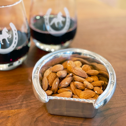 aluminum horseshoe shaped bowl with almonds in front of two stemless wine glasses with etched Saddlebred horse and horseshoe